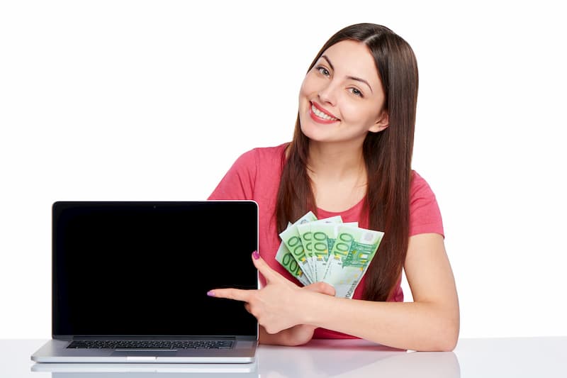 Eine Frau hält Geldscheine und zeigt auf einen Laptop