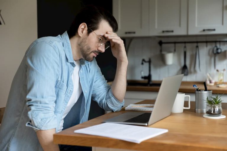 Ein junger Mann sitzt vor dem Laptop und denkt über das Schreiben einer Kündigung nach