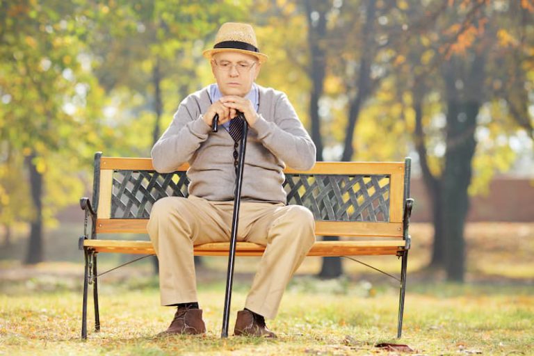 Ein alter Mann sitzt auf einer Parkbank und denkt über Grundsicherung nach