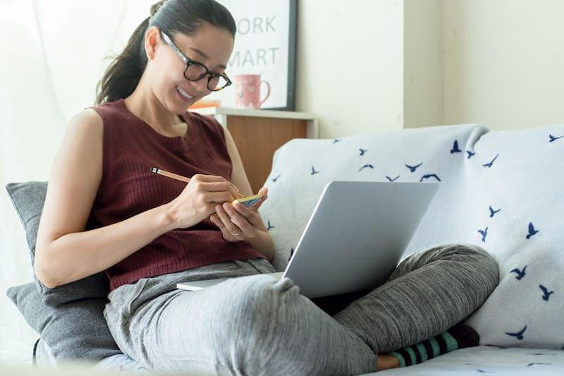 Eine Frau sitzt auf dem Sofa und arbeitet im Homeoffice mit Laptop auf dem Schoß