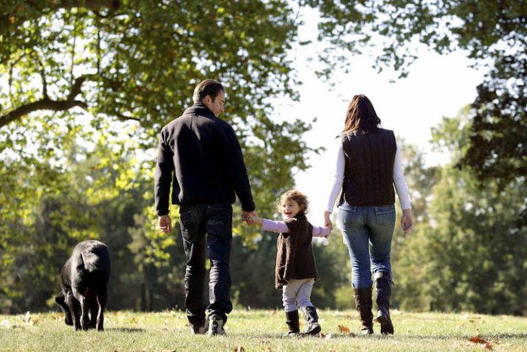 Eltern machen mit Kind und Hund einen Spaziergang, sie sind entspannt aufgrund des Elterngeldes