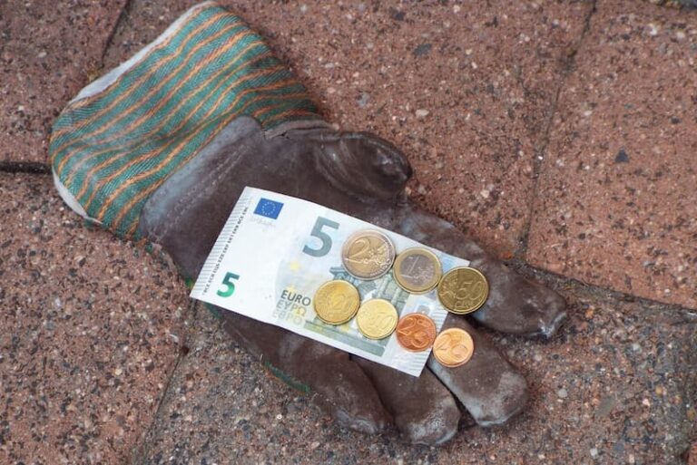 Ein Arbeitshandschuh mit Geldmünzen und einem Euroschein, Symboldbild für den Mindestlohn