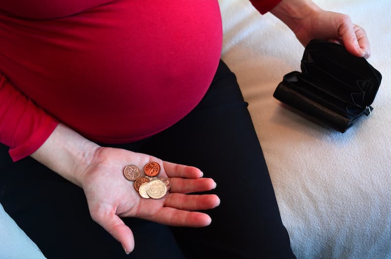 Eine schwangere Frau schaut auf Münzen, sie hat Anspruch auf Mutterschaftsgeld