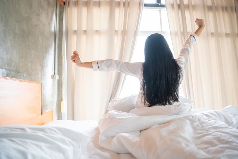 Eine Frau beim frühen Aufstehen, sie streckt sich im Bett