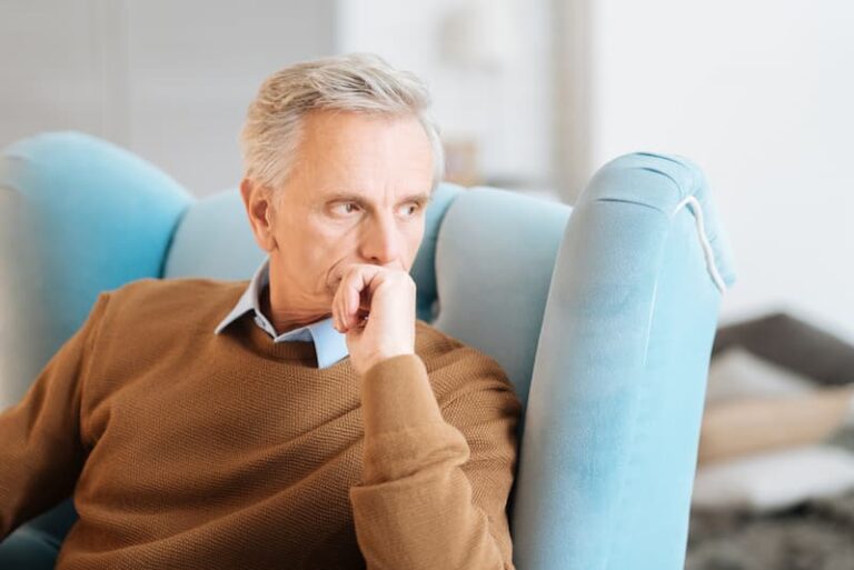 Ein alter Mann sitzt nachdenklich und gelangweilt auf einem Sessel, er leidet am Empty-Desk-Syndrom