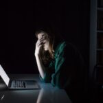 Eine Frau sitzt mit der Hand vor den Augen vor dem PC, sie erlebt Cybermobbing