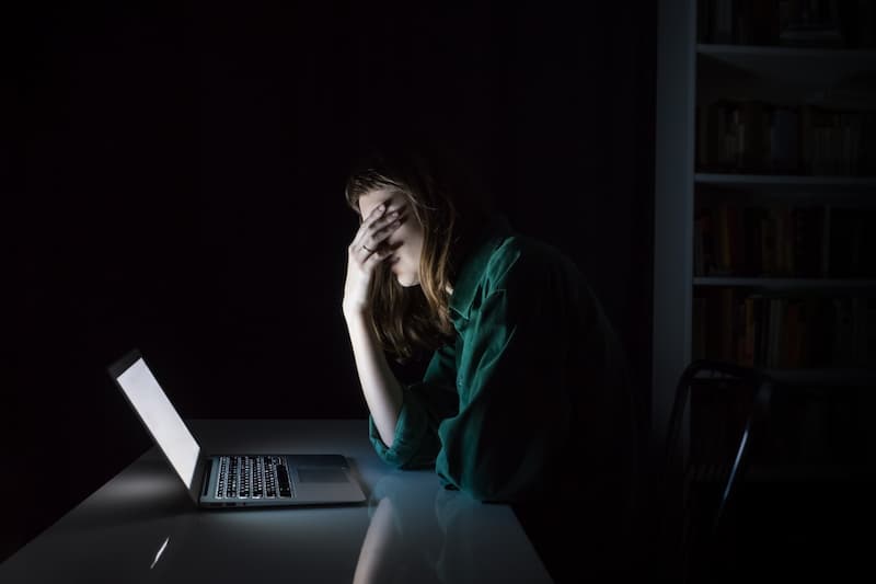Eine Frau sitzt mit der Hand vor den Augen vor dem PC, sie erlebt Cybermobbing