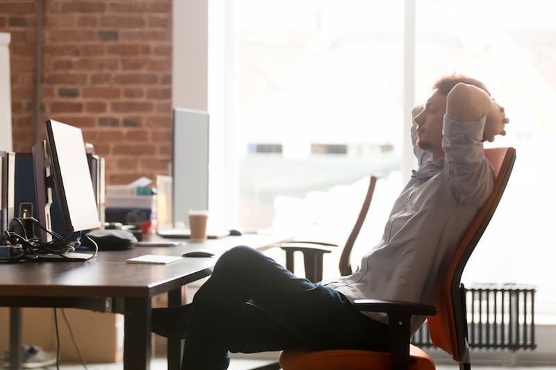 Ein Mann sitzt entspannt am Arbeitsplatz, wie entwickelt man Gelassenheit?