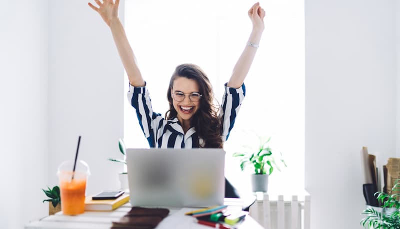 Eine Frau sitzt glücklich vor ihrem Laptop, was ist intrinsische Motivation?