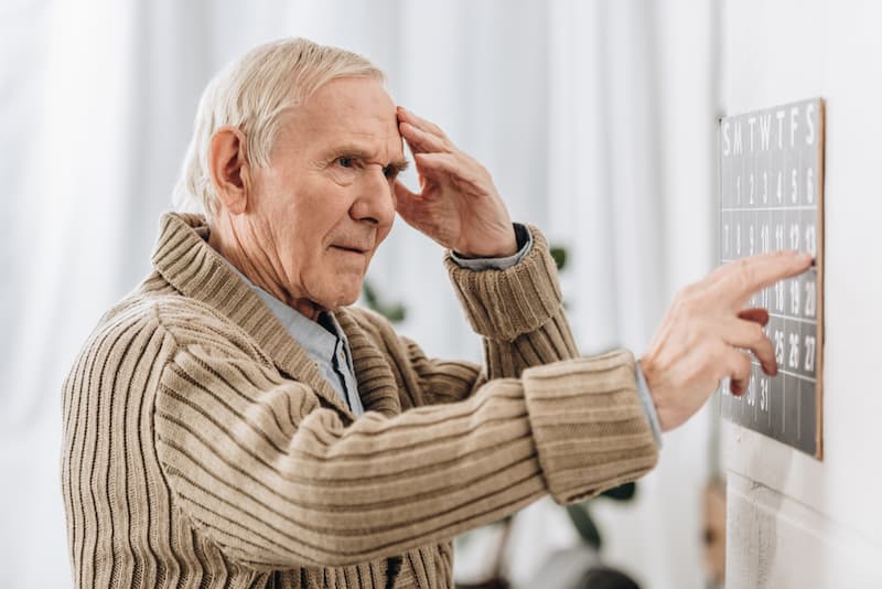 Ein älterer Mann blickt fragend auf einen Kalender, was ist Demenz?