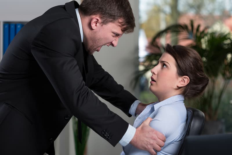 Ein Mann packt einer Frau an den Arm, was tun bei Gewalt am Arbeitsplatz?