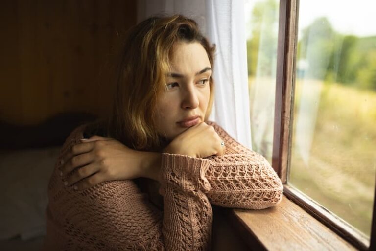 Eine Frau sitzt traurig am Fenster, sie empfindet keine Lebensfreude mehr