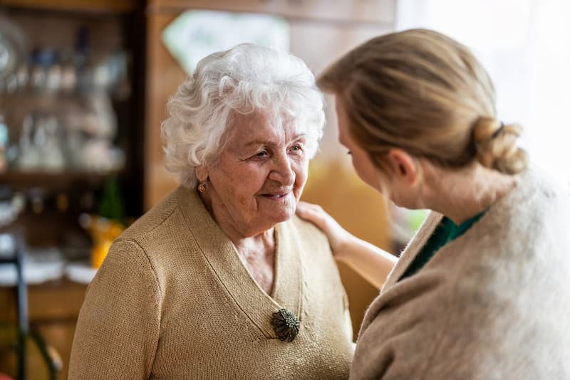 Eine Pflegekraft kümmert sich um eine alte Frau, wie lassen sich die Stufen der Pflegegrade richtig beantragen?