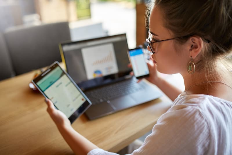 Eine Frau am Laptop mit zwei Smartphones in der Hand, ist Multitasking im Job sinnvoll?