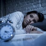 Eine Frau liegt wach im Bett, wie stoppt man das Gedankenkarussell?