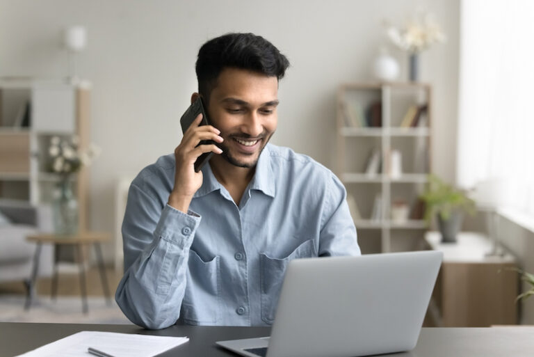 Freier Mitarbeiter arbeitet zu Hause am Laptop und telefoniert mit seinem Auftraggeber