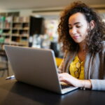 Eine zufriedene Studentin sitzt am Laptop und möchte ihre Studiengebühren absetzen.
