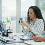 Vier Beschäftigte sitzen im Meeting am Tisch und schauen auf ihr Smartphone, dem Produktivitätskiller, anstatt sich zu unterhalten und zu arbeiten.