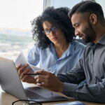 Im Rahmen des Offboarding-Prozesses erklärt ein Arbeitnehmer seiner Nachfolgerin seine Aufgaben am Laptop.