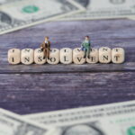 Zwei Figuren, Männer im Anzug darstellen, sitzen auf Würfeln, die das Wort "insolvent" darstellen. Ein Symbolbild für Insolvenzgeld.