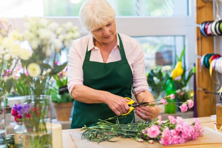 Eine selbstständige Floristin gehobenen Alters bindet einen Blumenstrauß. Sie hat eine gute Altersvorsorge bei Selbstständigkeit.