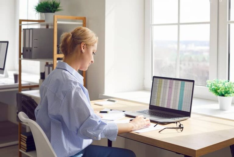 Eine Frau sitzt am Laptop und nutzt digitale Kompetenzen, um eine Tabelle auszuwerten.
