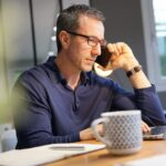 Ein Mann arbeitet zu Hause am Laptop und telefoniert. Er übt als Texter und Lektor Jobs für Einzelgänger aus.
