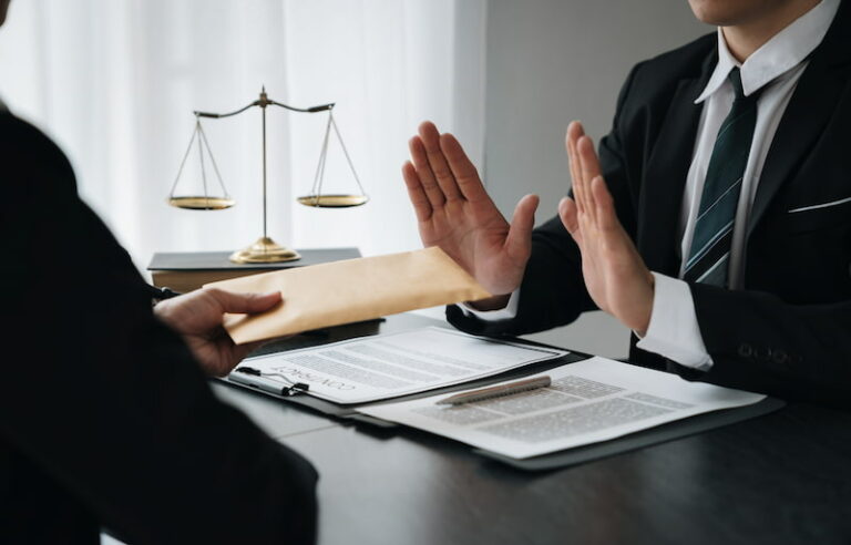 Ein Geschäftsmann hebt gegenüber einem anderen Mann abwehrend die Hände, der ihm einen Briefumschlag überreichen möchte. Er lehnt aus Gründen der Moral und Ethik eine Bestechung ab.