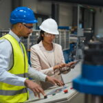 Ein Fabrikmitarbeiter erhält an einer Maschine Arbeitsanweisungen von seiner Vorgesetzten.