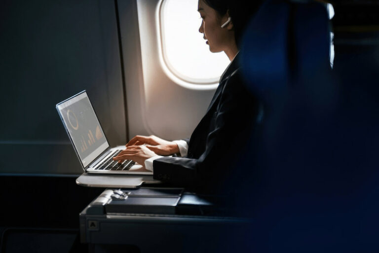 Eine Geschäftsfrau sitzt im Flugzeug und arbeitet im Laptop. Sie ist auf Dienstreise. Dafür benötigt sie die A1-Bescheinigung.