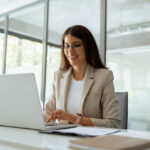 Eine Geschäftsfrau arbeitet am Laptop und lächelt. Sie nutzt Business Intelligence zur Datenanalyse. Was ist Business Intelligence?