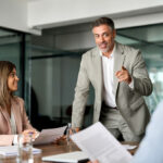 Ein Vorgesetzter im Anzug informiert seine Mitarbeitenden im Meeting über neue Vorschriften. Was ist Compliance-Management?