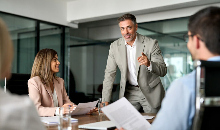 Ein Vorgesetzter im Anzug informiert seine Mitarbeitenden im Meeting über neue Vorschriften. Was ist Compliance-Management?